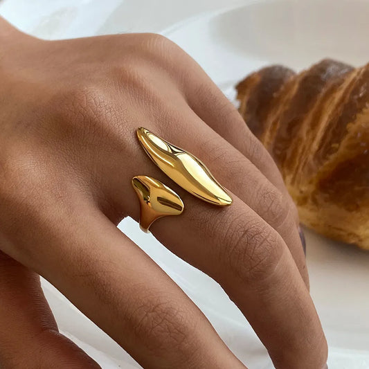 Close-up of a hand wearing a gold sculptural open band ring with fluid, asymmetrical design
